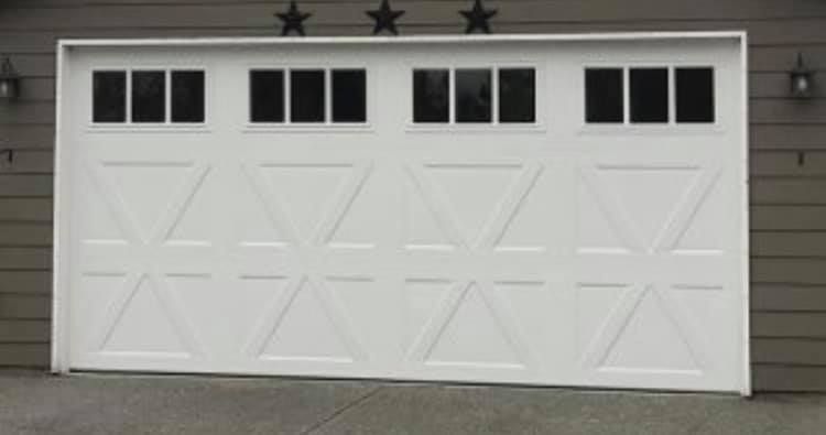 Wide steel carriage house garage door with X-brace panels and square windows on a tan home