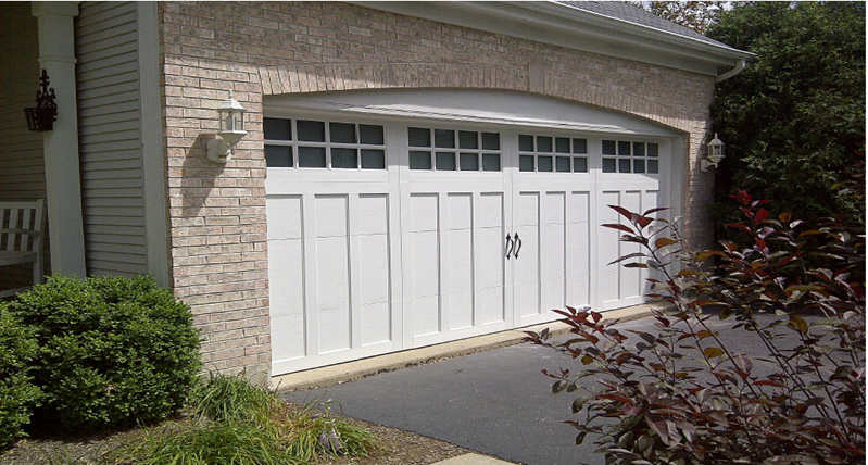 Brick home with a white steel carriage house garage door, square window panes, and an arched brick surround