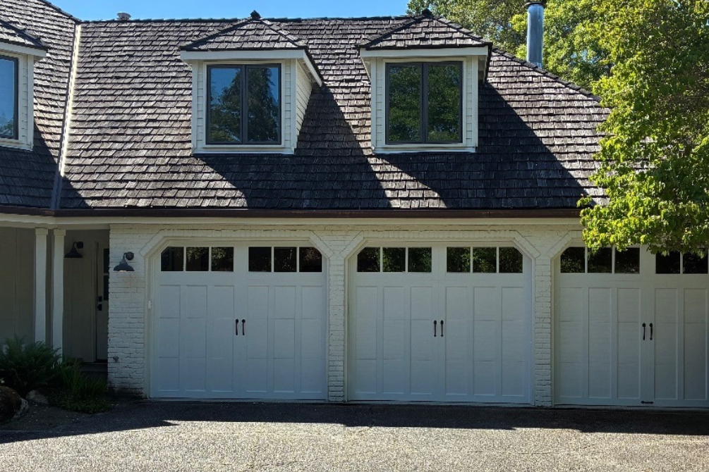 Three white steel carriage house garage doors with square windows and black handles on a white brick home