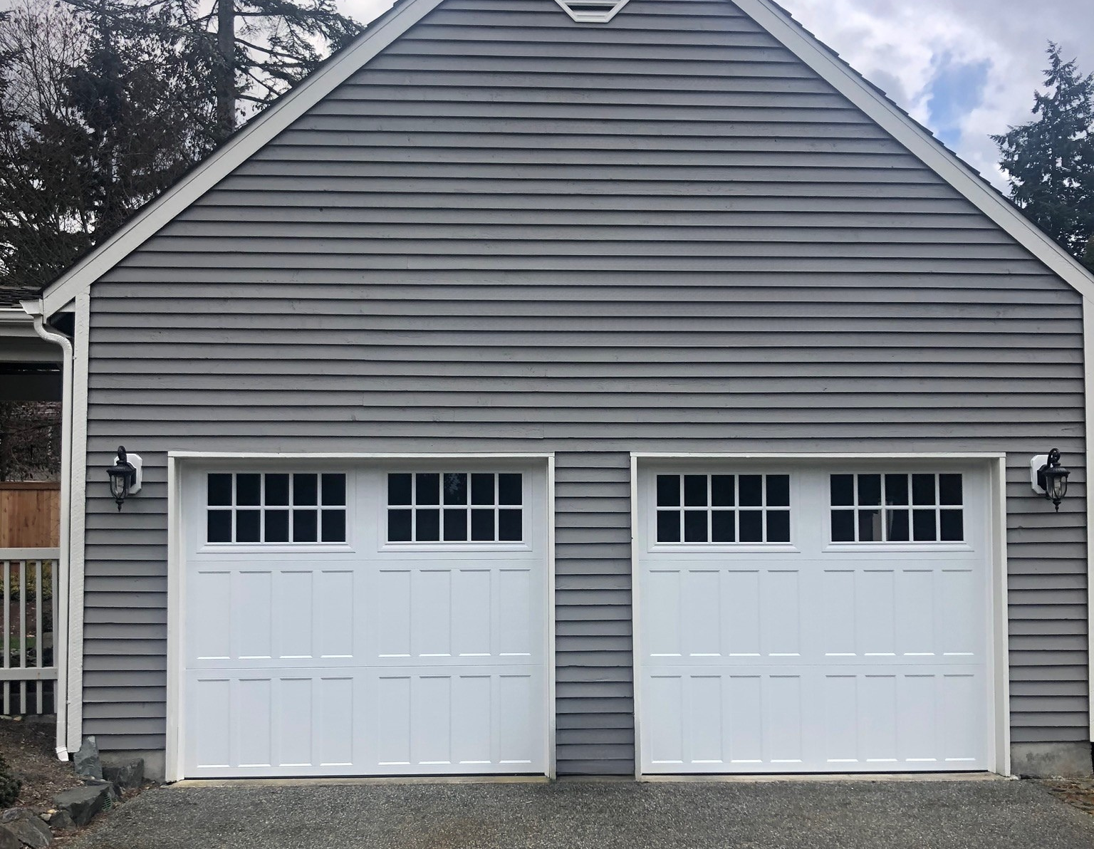 Two white steel carriage house garage doors with square windows on a gray home