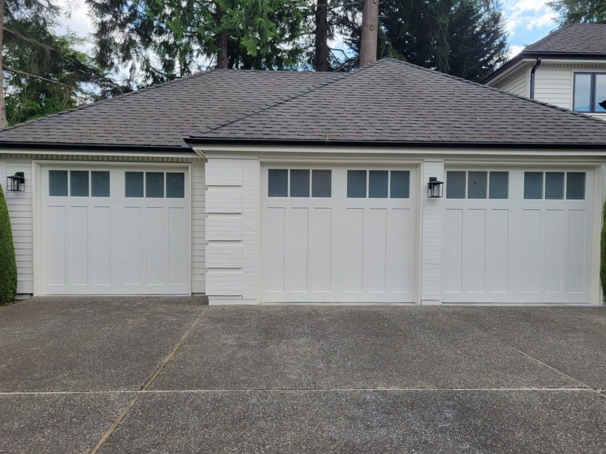 White steel carriage house garage doors with square windows beneath an extended roofline on a tan home
