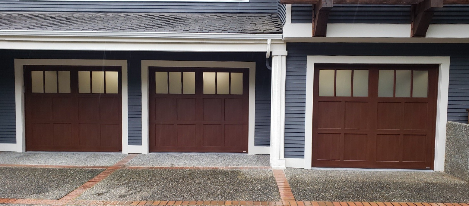 Navy blue home with three dark wood-tone steel carriage house garage doors, square window panes, and a brick paver driveway