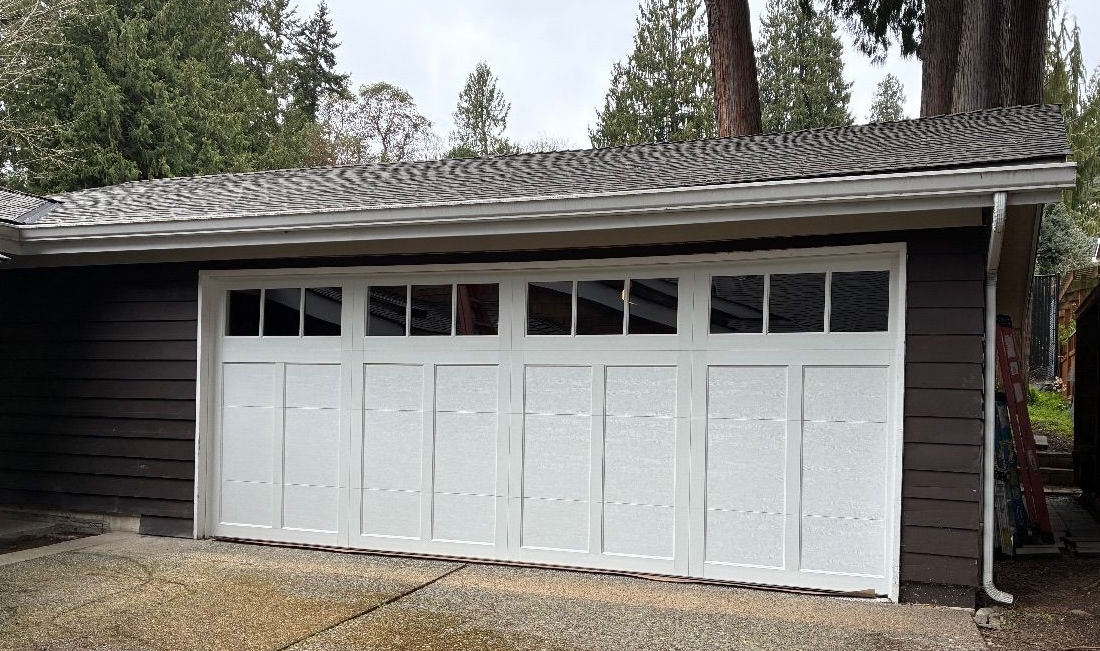 Dark brown home with a wide white steel carriage house garage door, square window panes, and a stone accent wall