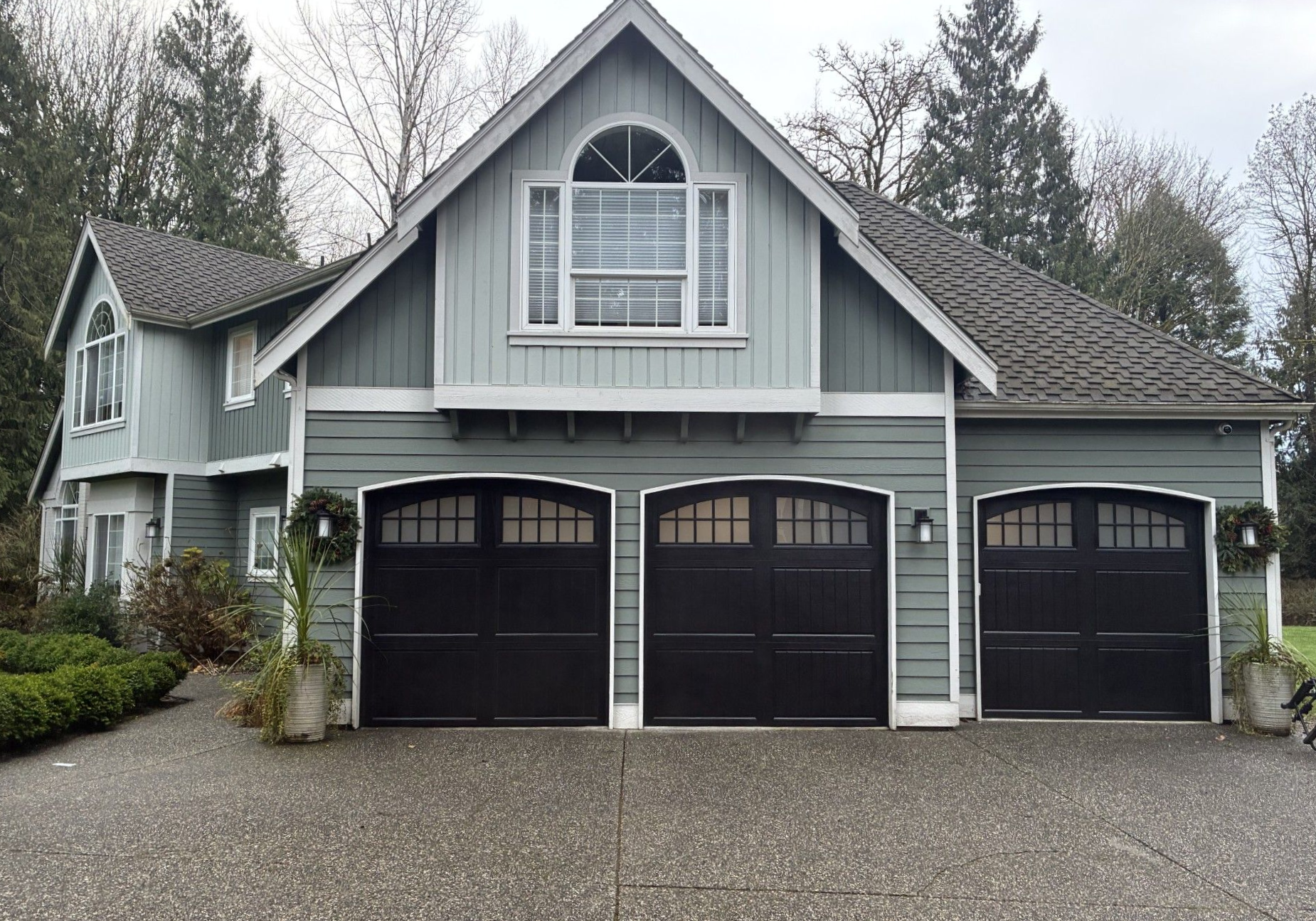 Two-story gray home with three black arched steel carriage house garage doors and a dormer window