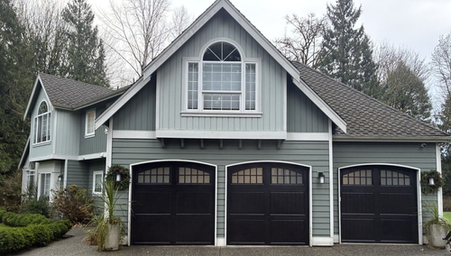 Steel carriage-style garage doors with arched windows on a gray home