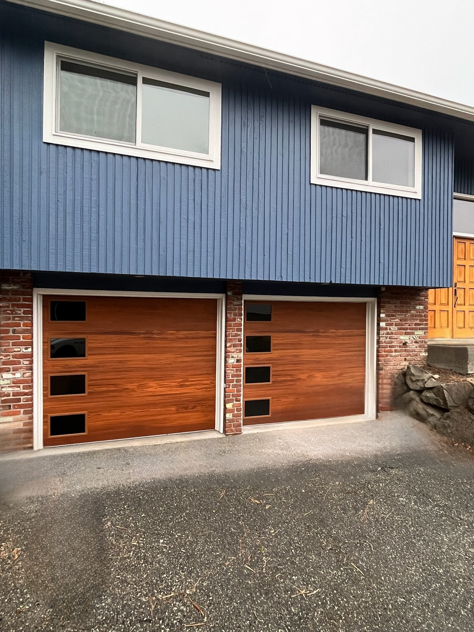 Wood-tone garage door with window accents on a brick home
