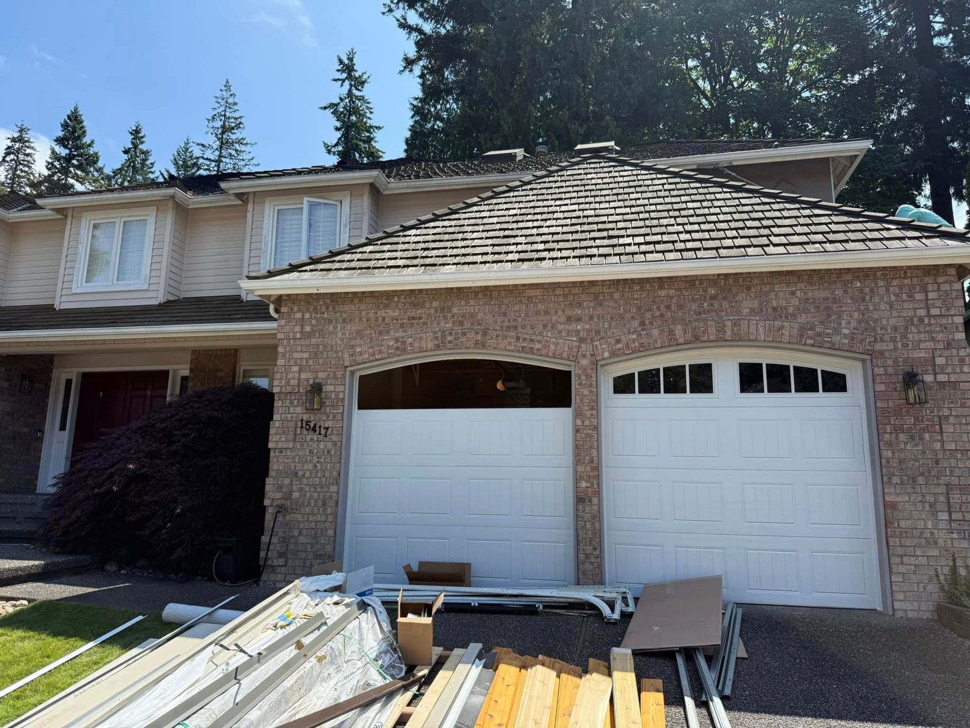 Garage door installation in progress on a brick home with white raised-panel doors