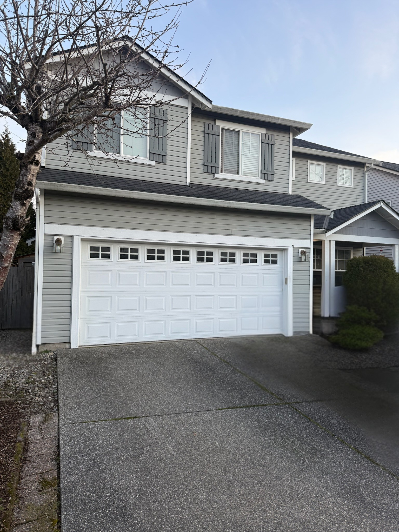 White traditional steel garage door with square windows on a gray two-story home