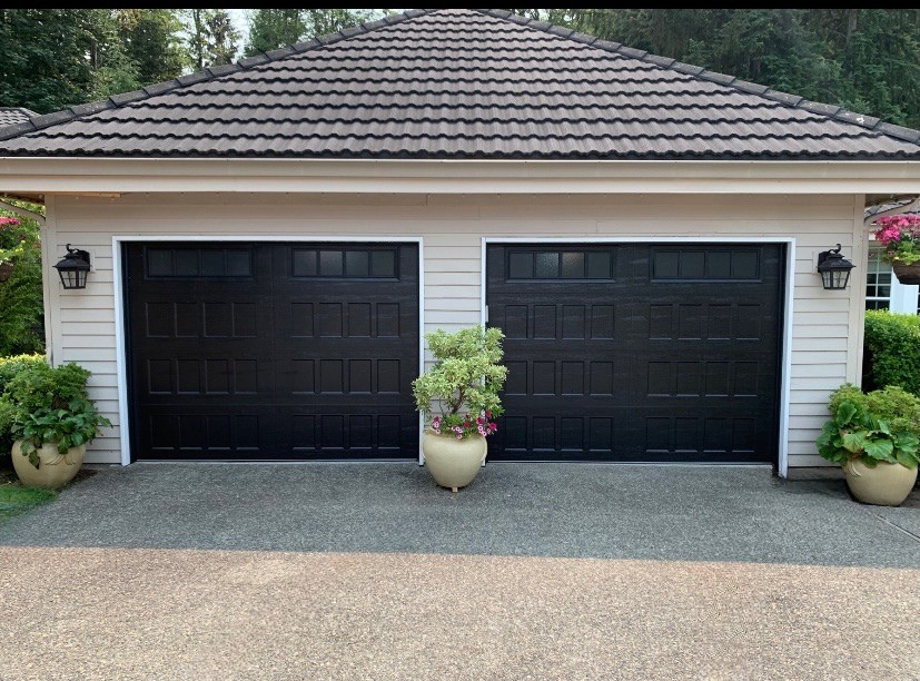Two black raised-panel steel garage doors with rows of small windows on a tile-roofed home