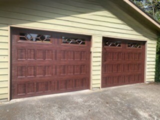 Reddish-brown traditional steel garage doors with fan-pattern windows on a tan home