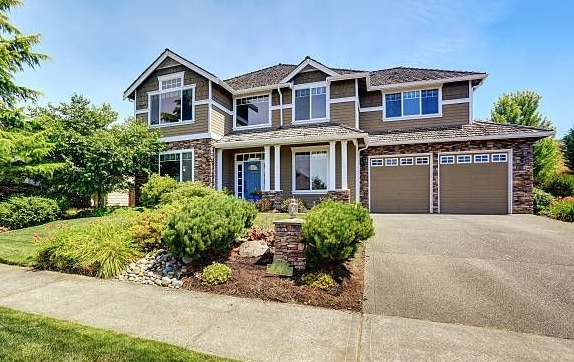 Two brown steel garage doors with raised panels and small square windows on a two-story craftsman-style home