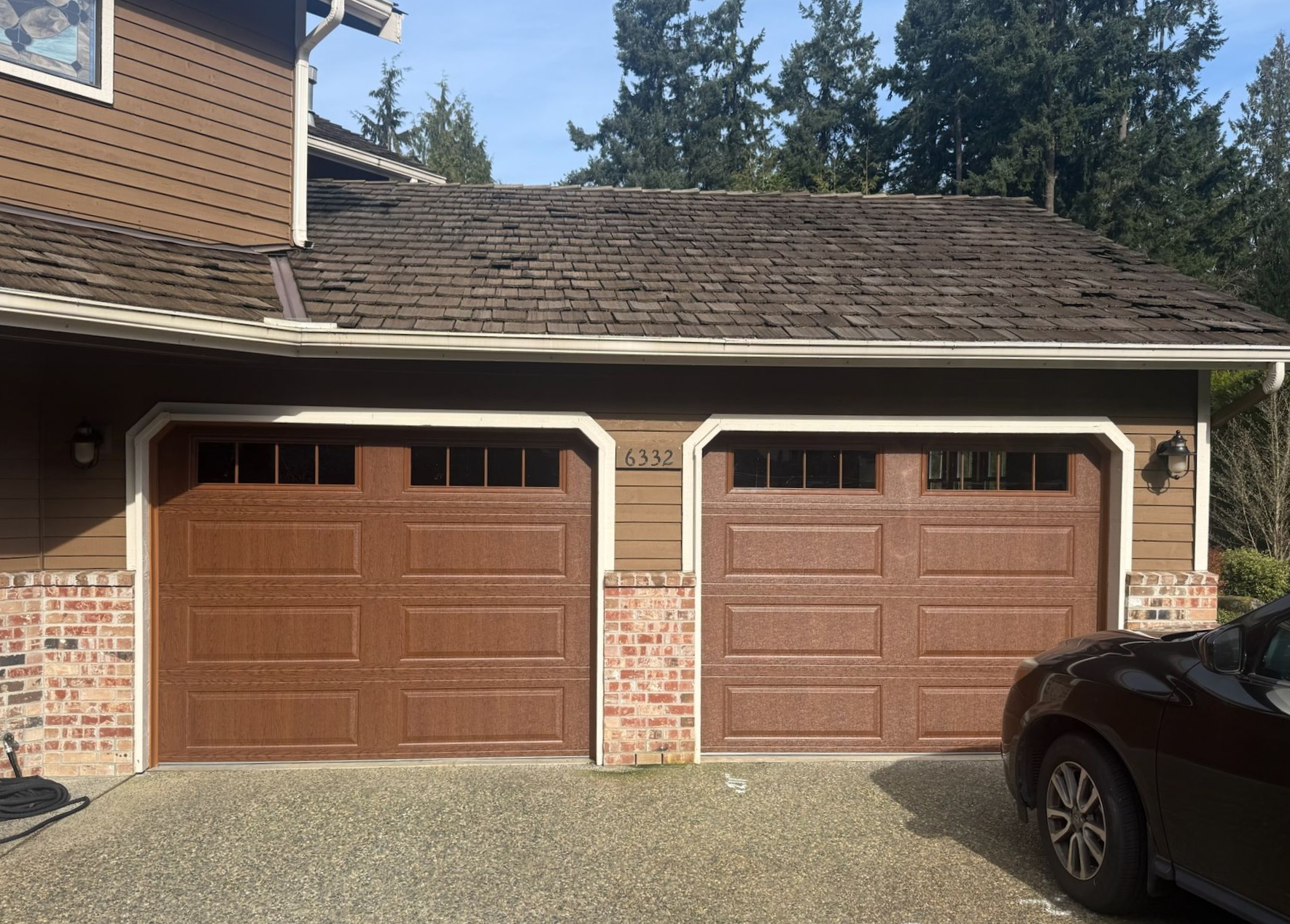 Wood-grain arched traditional steel garage doors with diamond-pane windows on brick