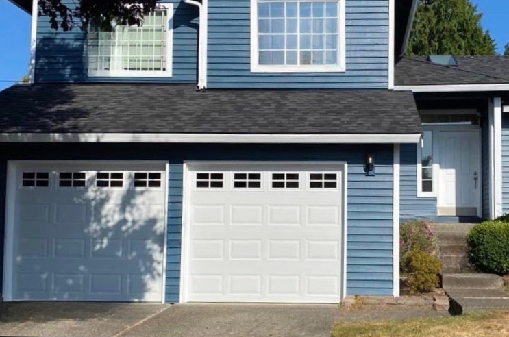 Two white traditional steel garage doors with rectangular windows on a blue home