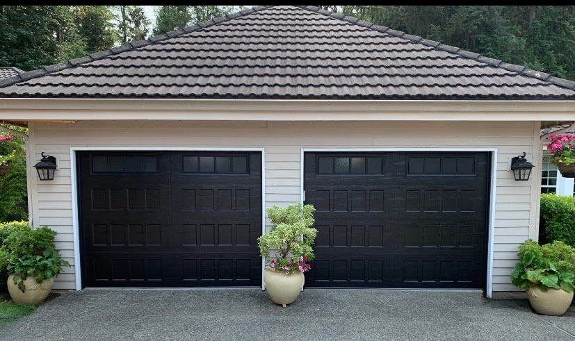 Black traditional steel garage doors with square windows on a brick facade