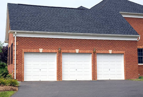 Three white traditional steel garage doors on a red-brick colonial home