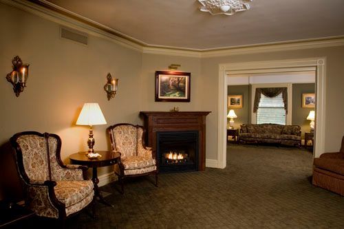 A living room with a fireplace , chairs , lamps and a couch.