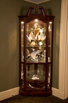 A corner curio cabinet is sitting in a corner of a room.