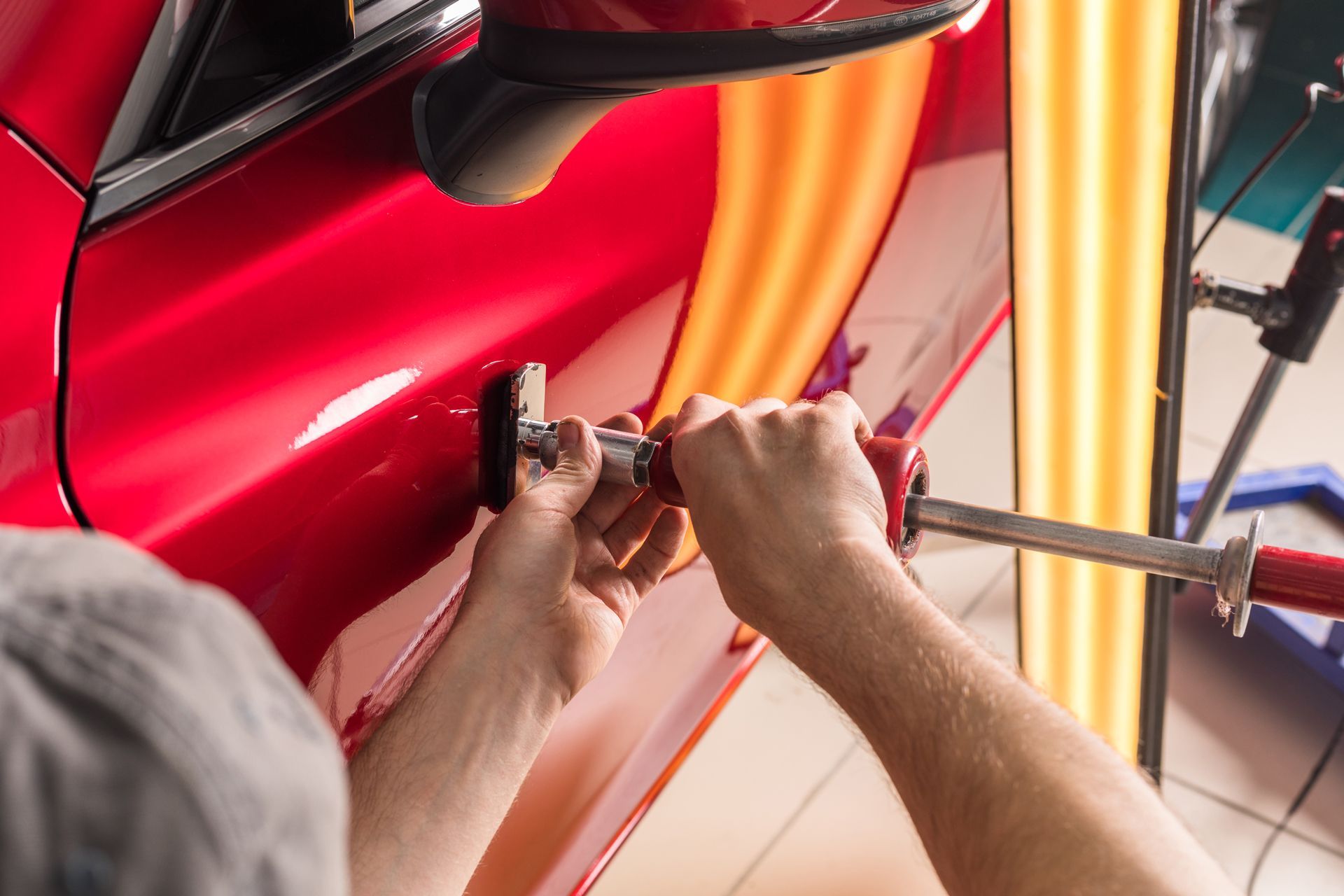 a man is working on a red car door removing dents
