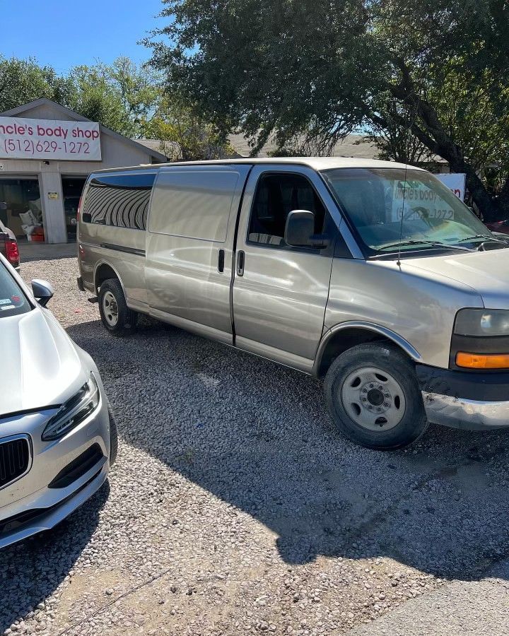 A silver van is parked next to a white car in a gravel lot.