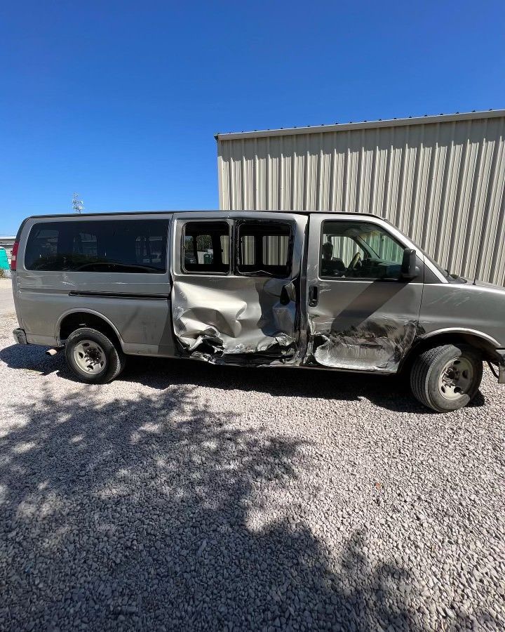 A damaged van is parked in a gravel lot in front of a building.