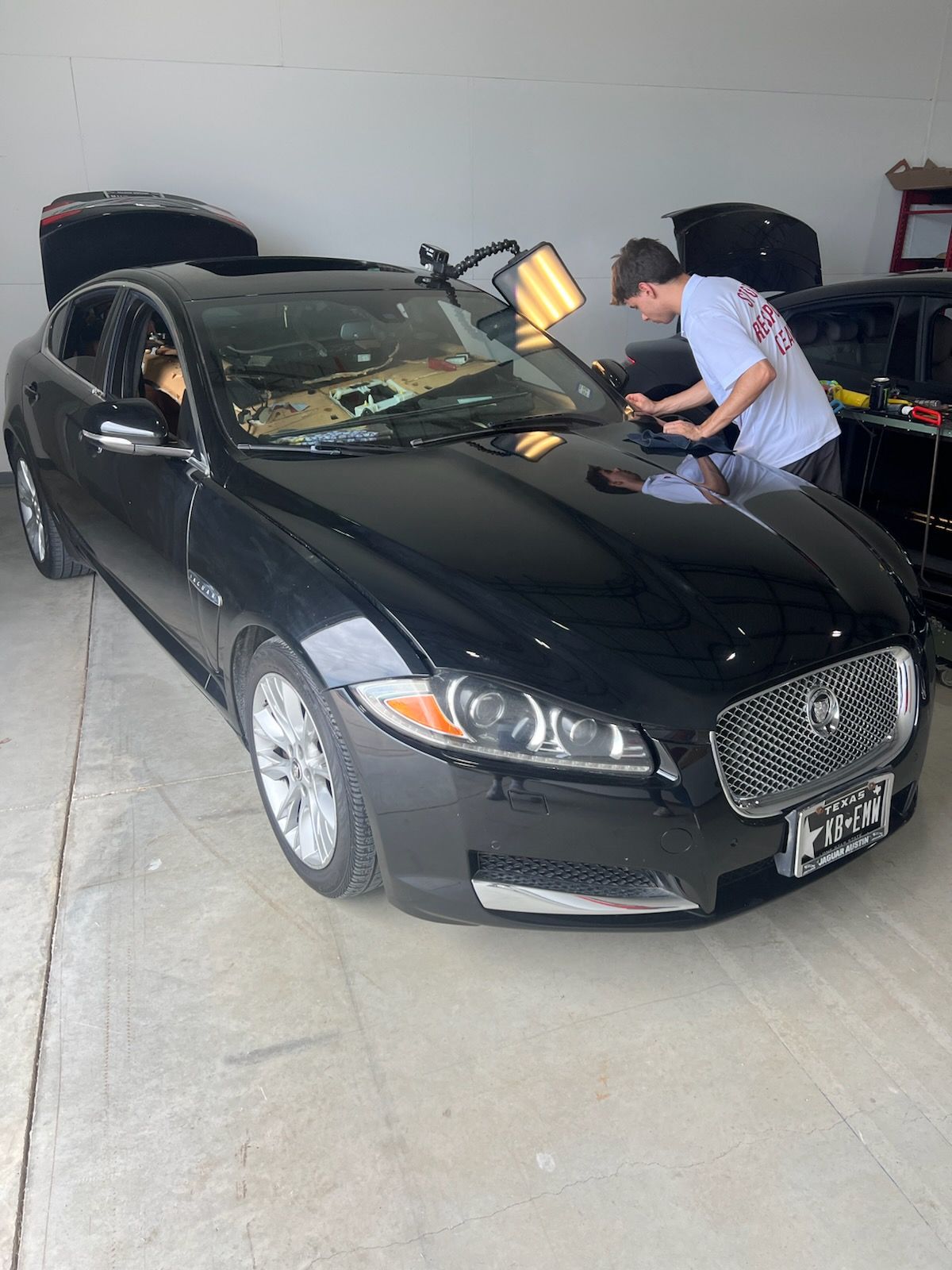 A man working on a black Jaguar in a garage; using tools to repair the car's body.