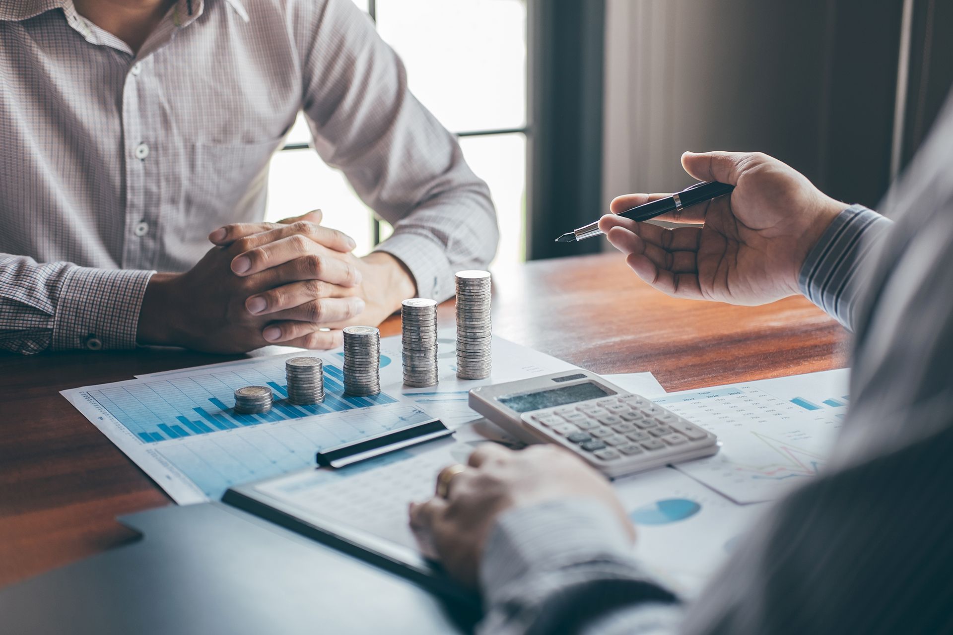 Two men are sitting at a table talking about money.