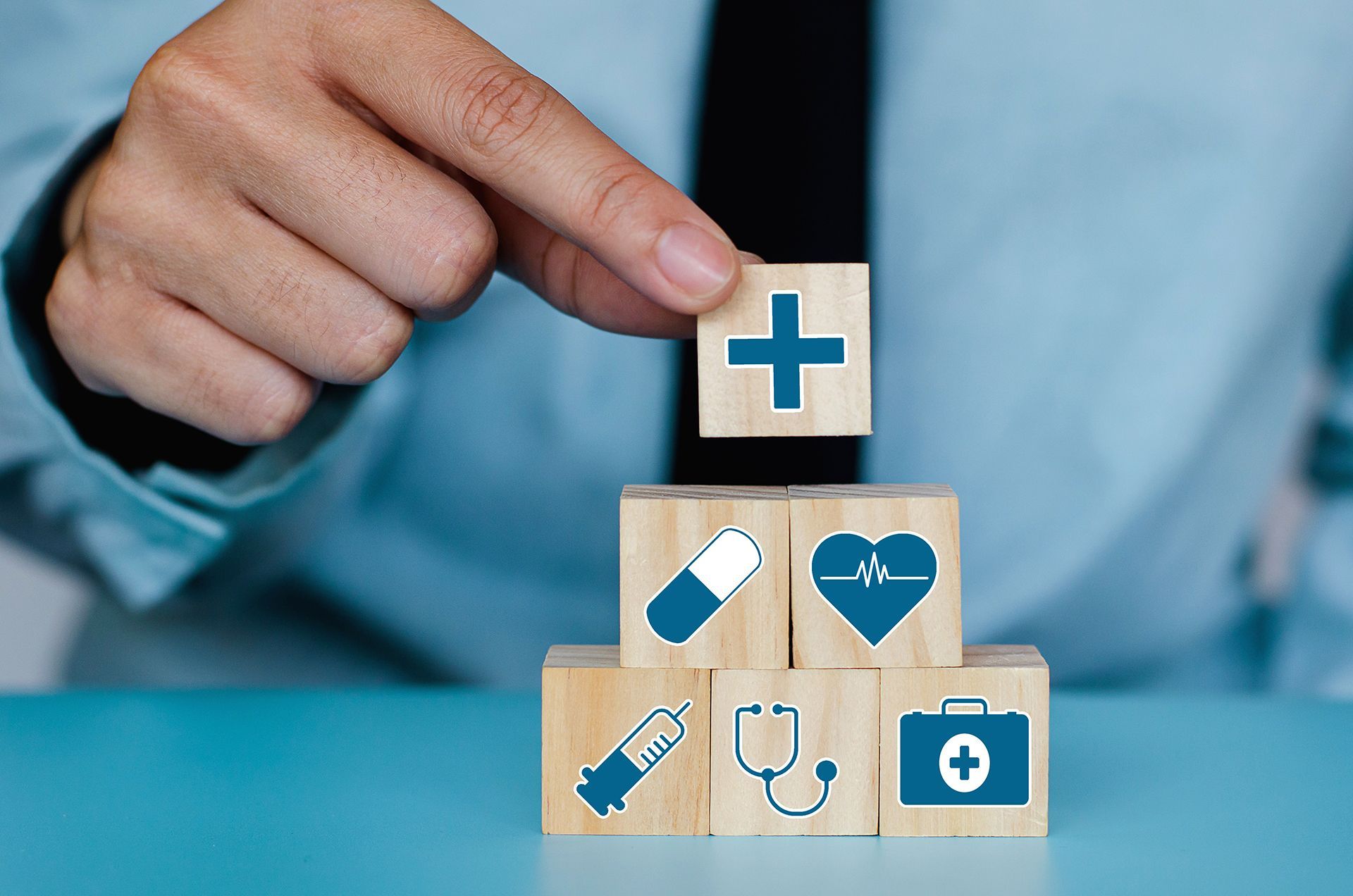 A person is stacking wooden blocks with medical icons on them.
