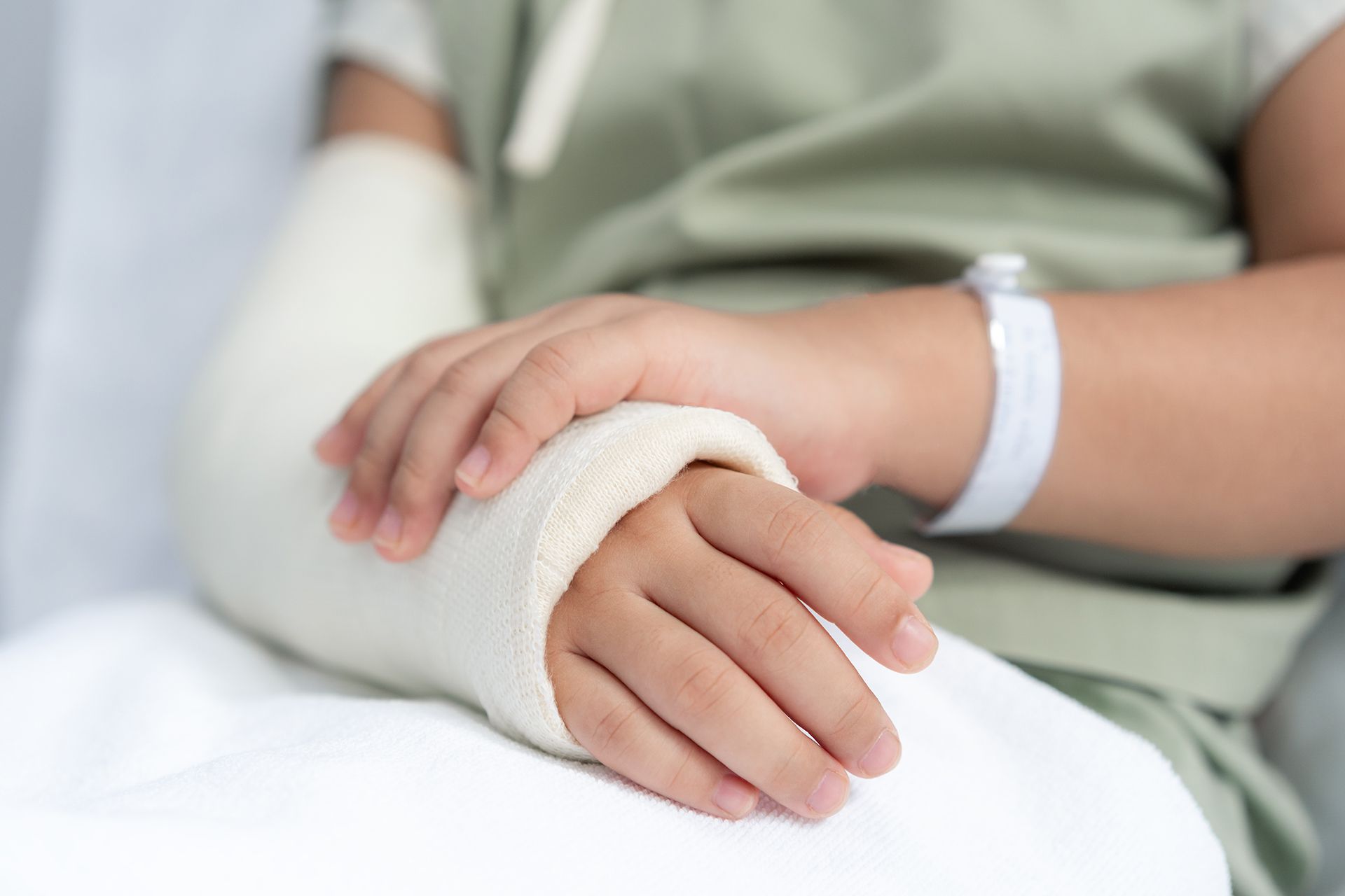 A child with a cast on their arm is sitting in a hospital bed.