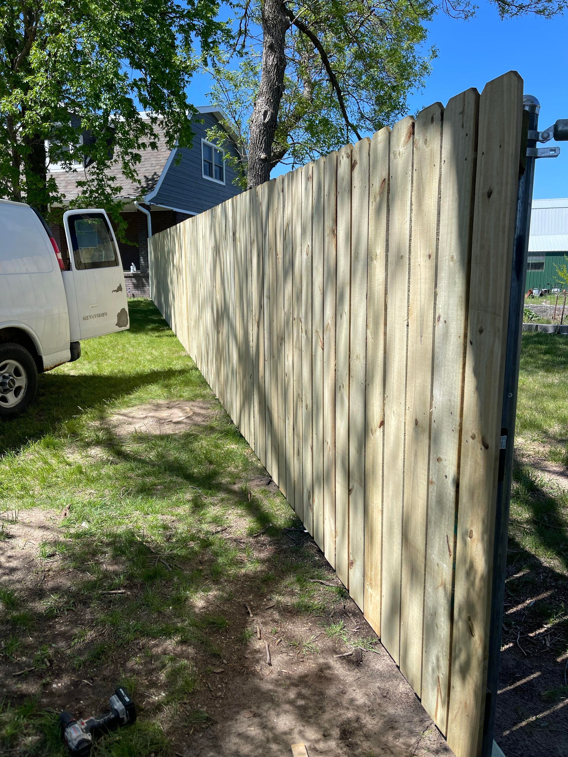 Wooden privacy fence beside a white van on a sunny residential lot