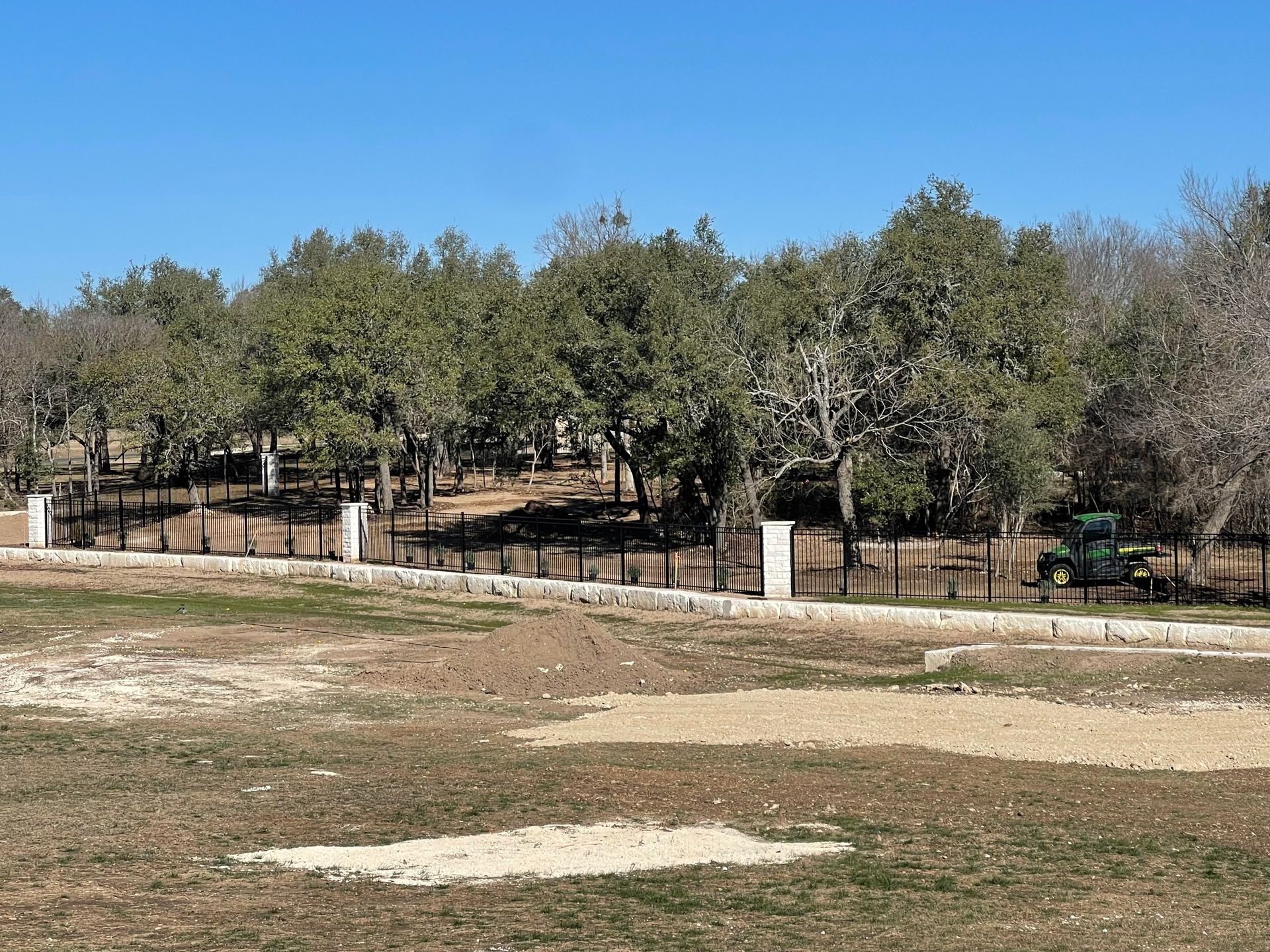 Open grassy field with trees, fence, and a clear blue sky