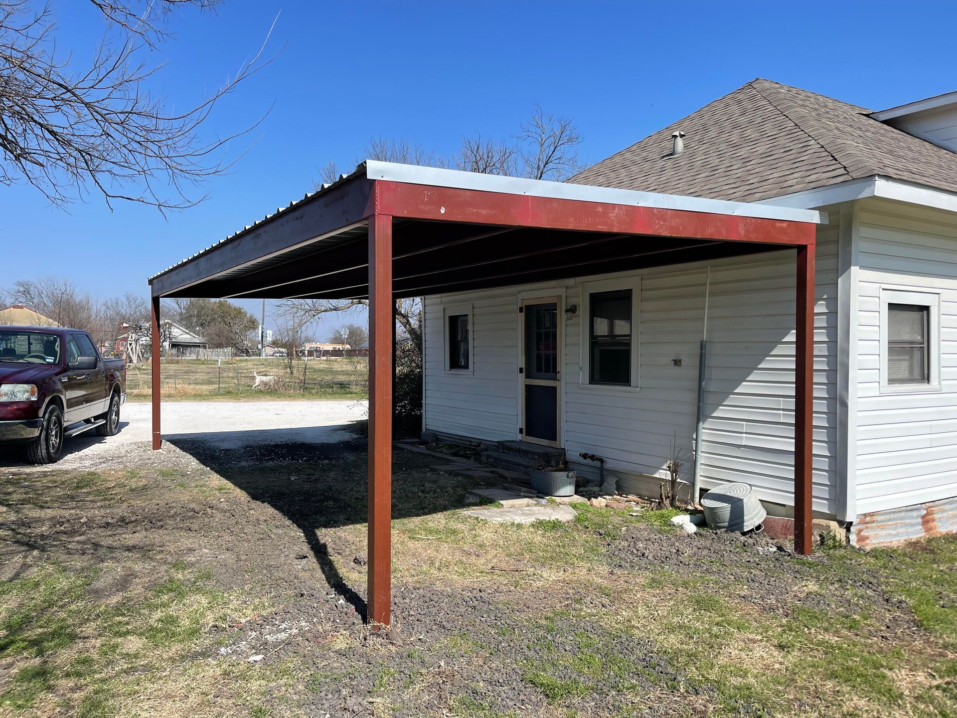 Small house with a red metal carport and light gray siding in a grassy yard.