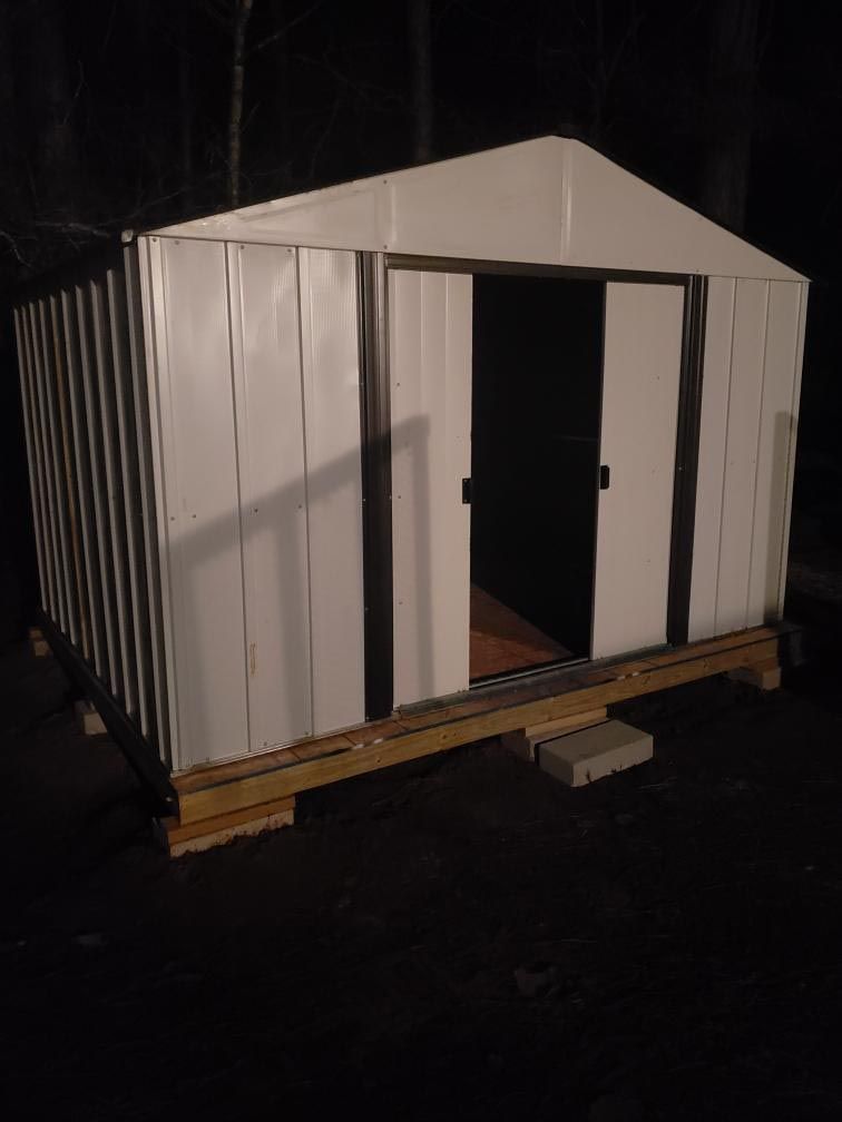 Small white metal shed with open double doors on a wooden base at night