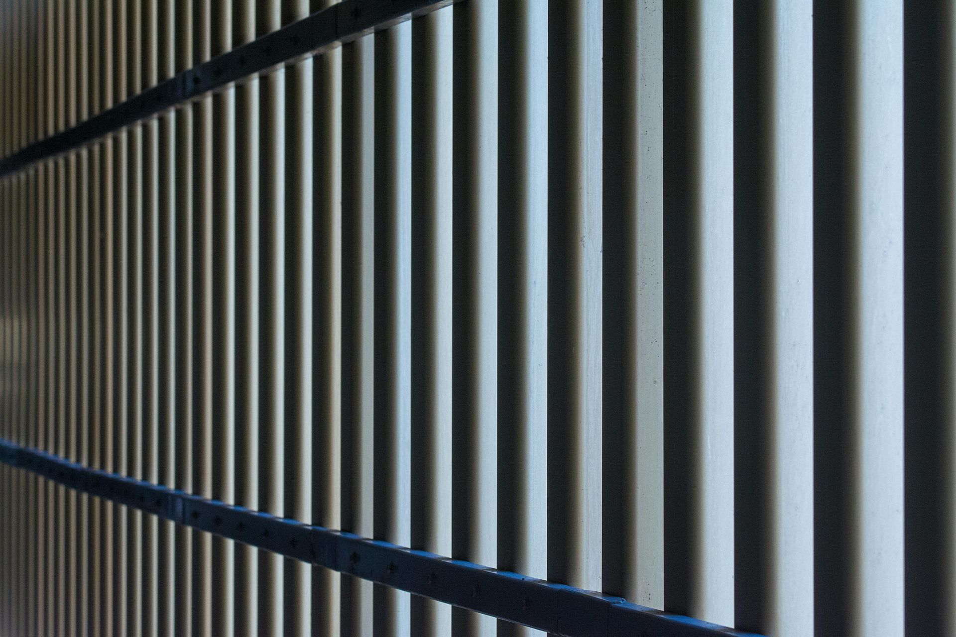 Diagonal view of vertical metal bars casting shadows in a dim corridor