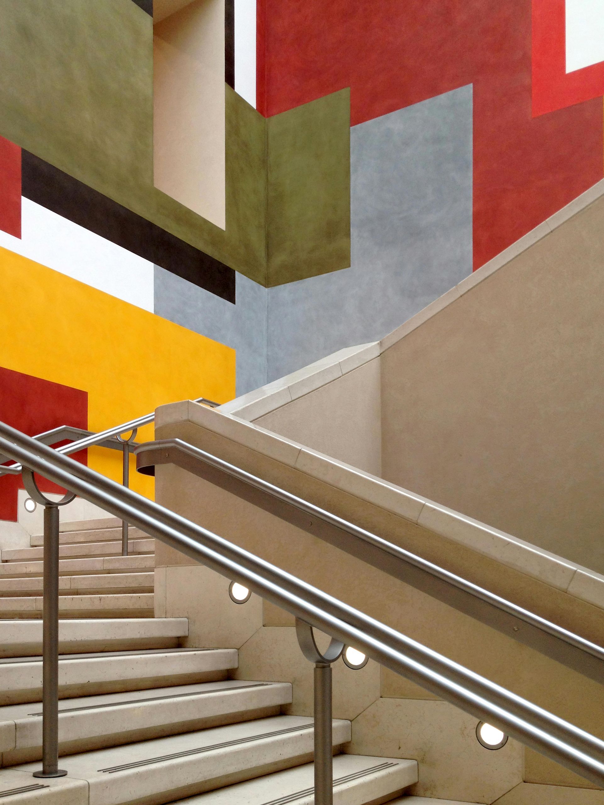 Stairwell with beige steps, metal handrails, and colorful geometric wall art in red, yellow, and green.