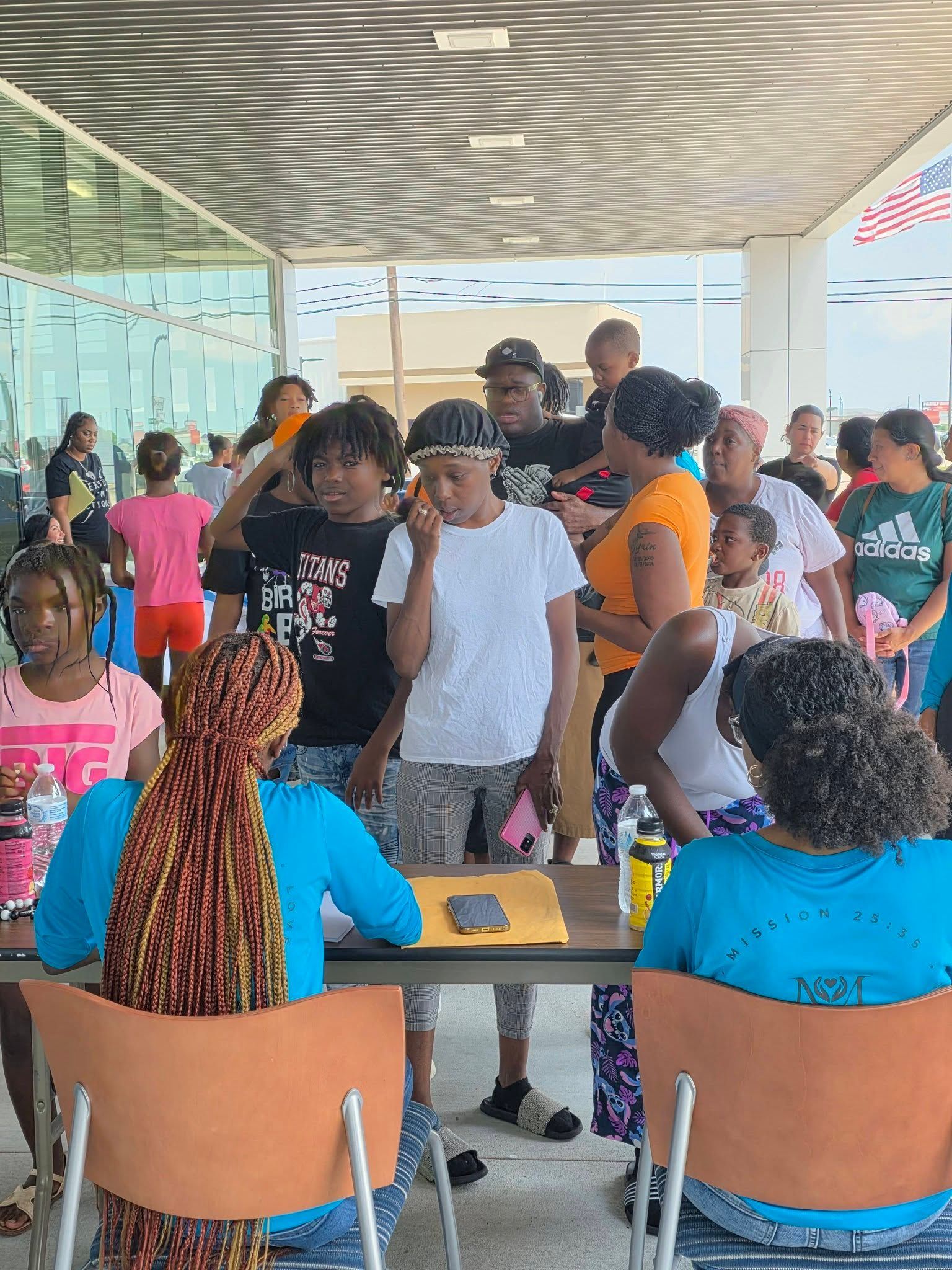 A registration desk outdoors with people standing in line for check-in under a covered building entrance.