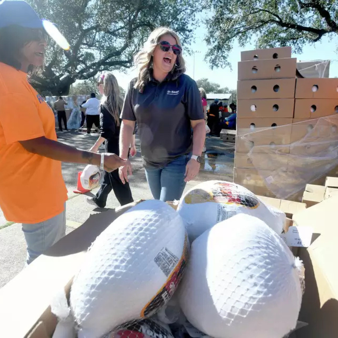 Volunteers distribute frozen turkeys from boxes at an outdoor community food donation event.