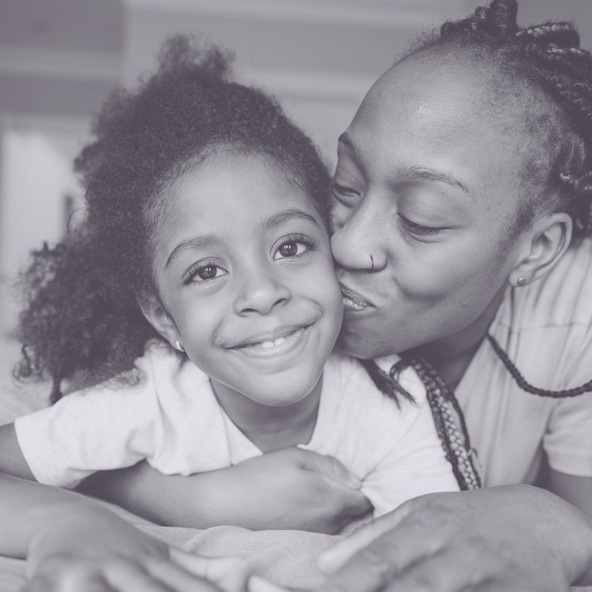 A person leans in to kiss a smiling child on the cheek while holding them in a close embrace.