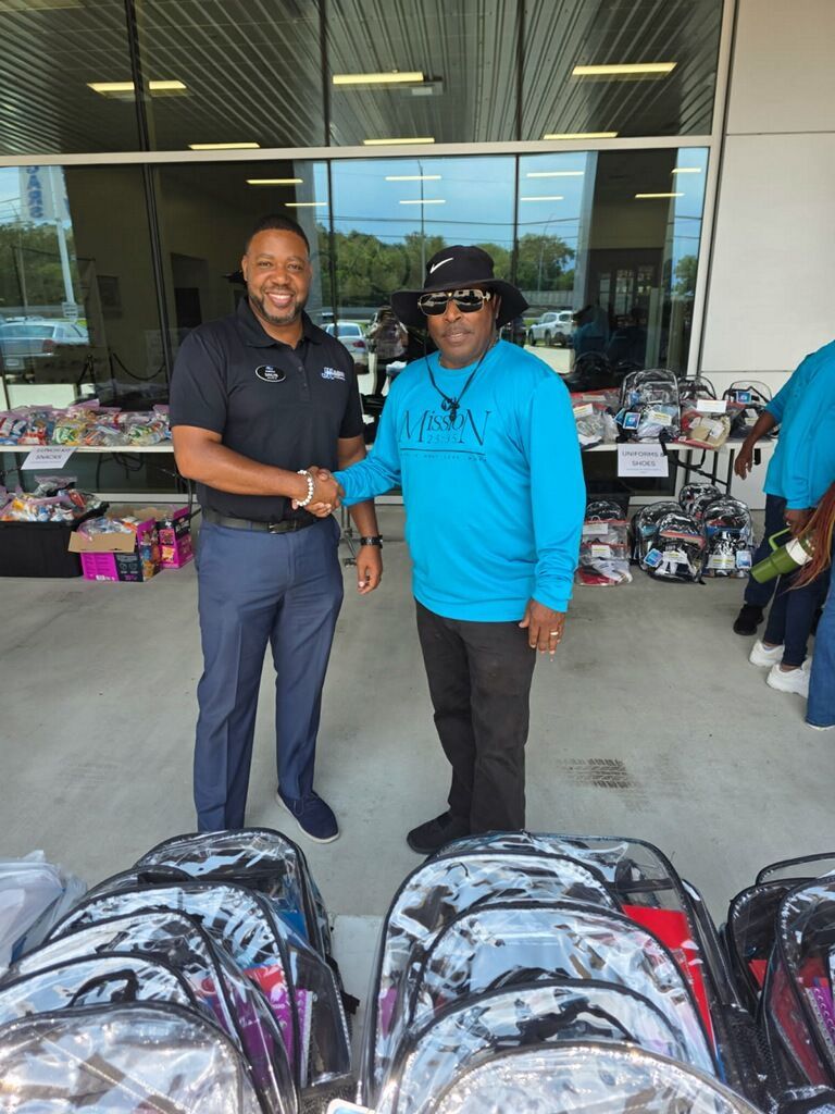 JK Subaru Leadership & Mission 2535 Board President shaking hands in front of a store display with backpacks and donated items.