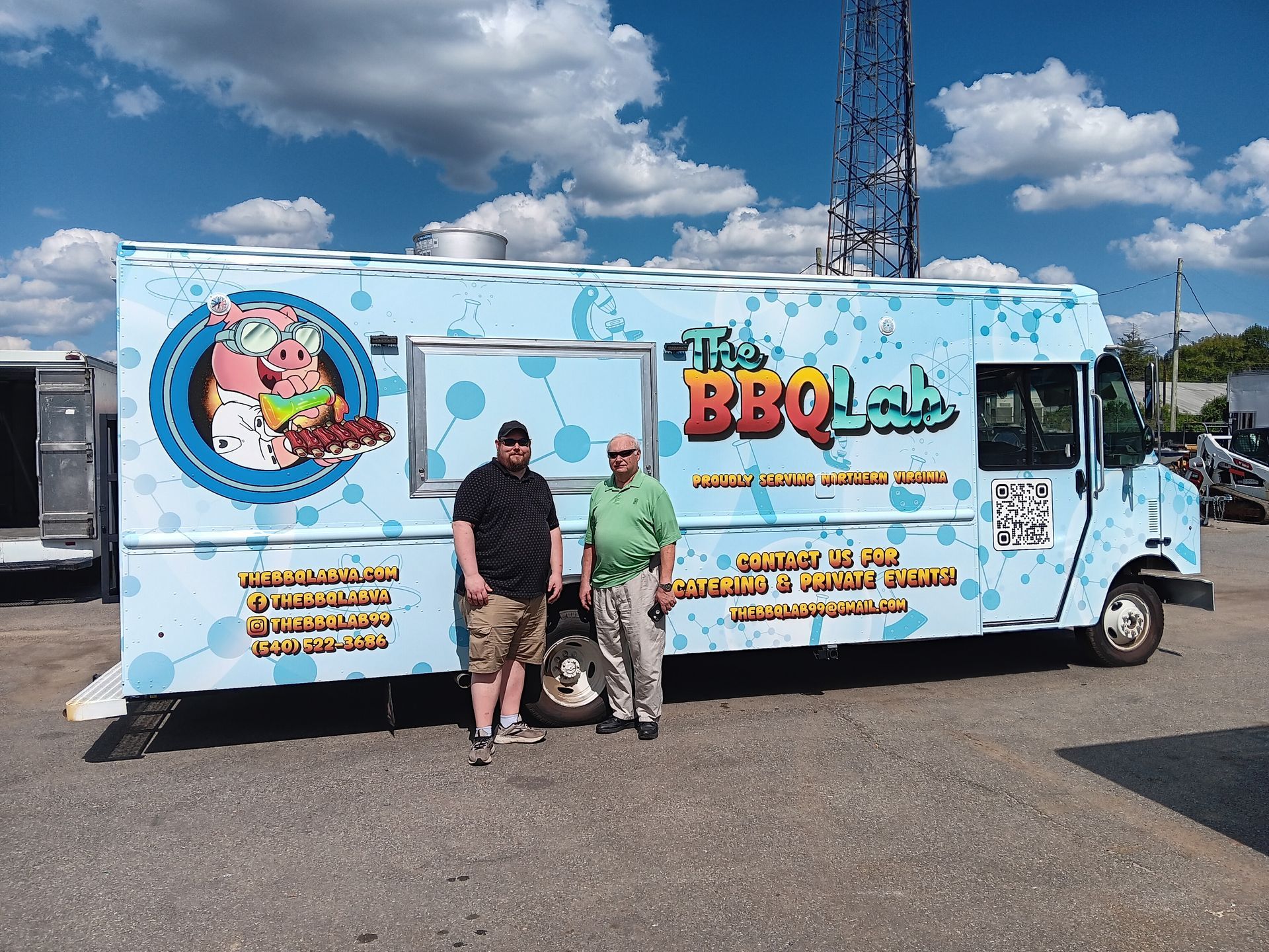 Two men stand in front of a blue food truck called