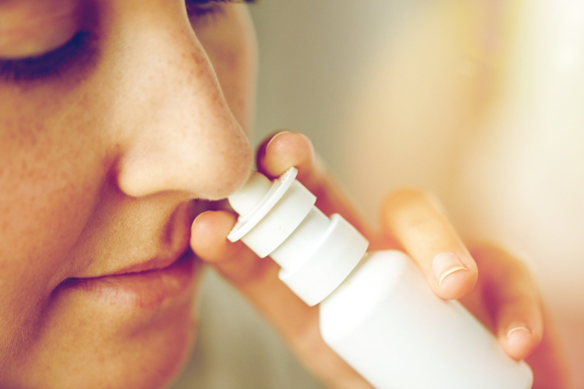 Person using a nasal spray, aiming the nozzle into their nostril. Close up.