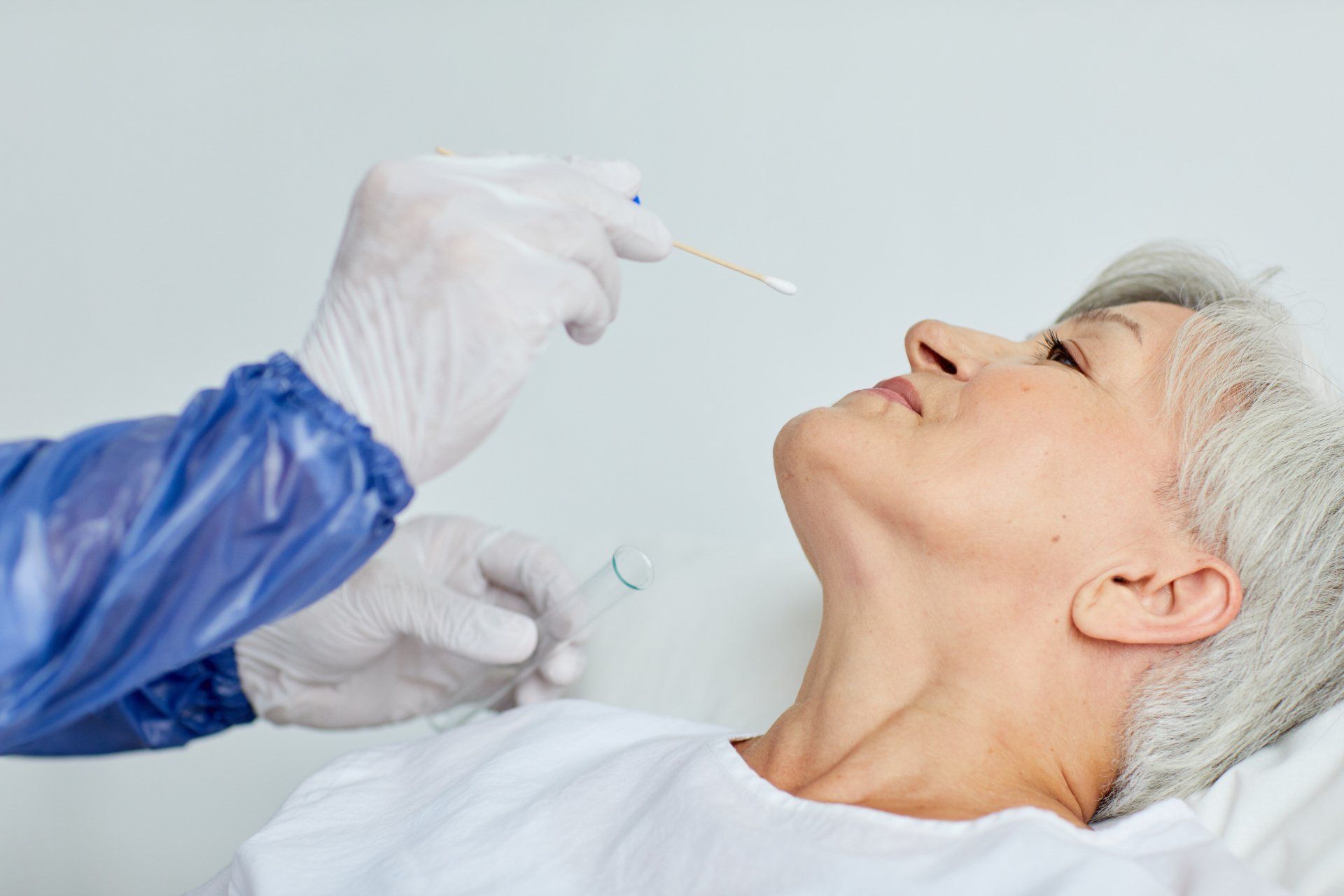 Person in bed receiving a nasal swab test from a person in PPE.