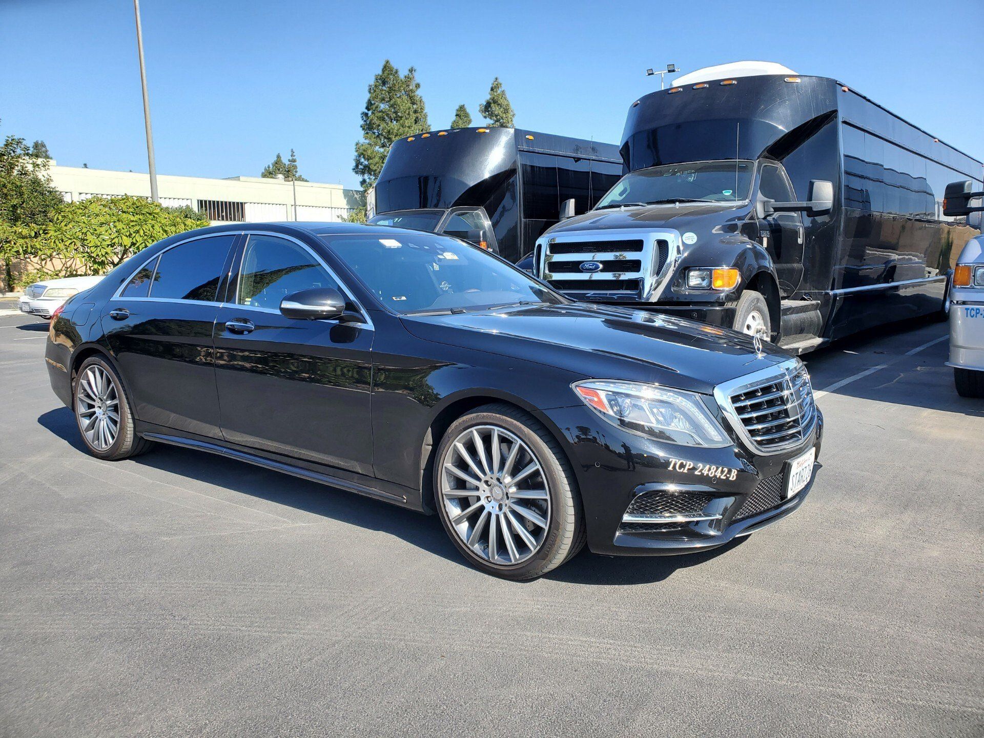 A black mercedes benz s class is parked in a parking lot next to a bus.