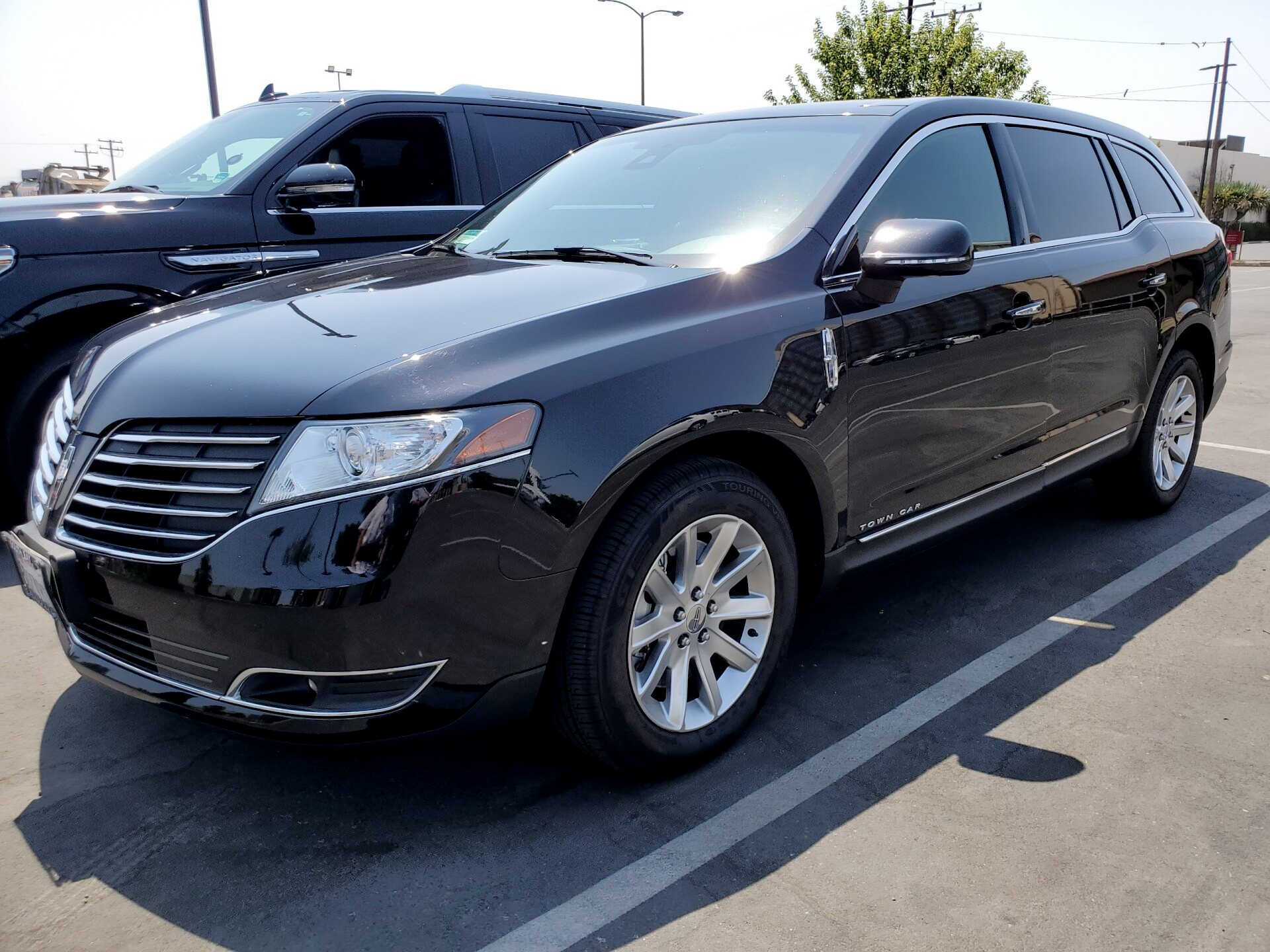 A black car is parked in a parking lot next to a black suv.