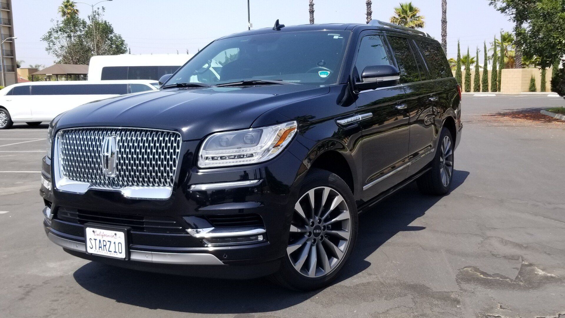 A black lincoln navigator is parked in a parking lot next to a white limousine.