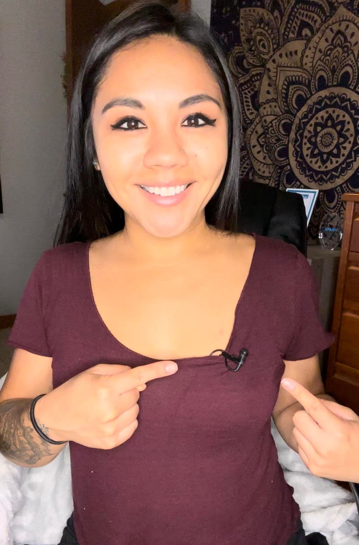 A woman in a purple shirt is pointing at her chest.