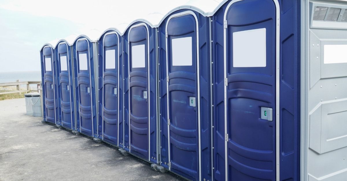 A row of brand-new portable toilet units. The row sits outside a production shoot for guests to use.