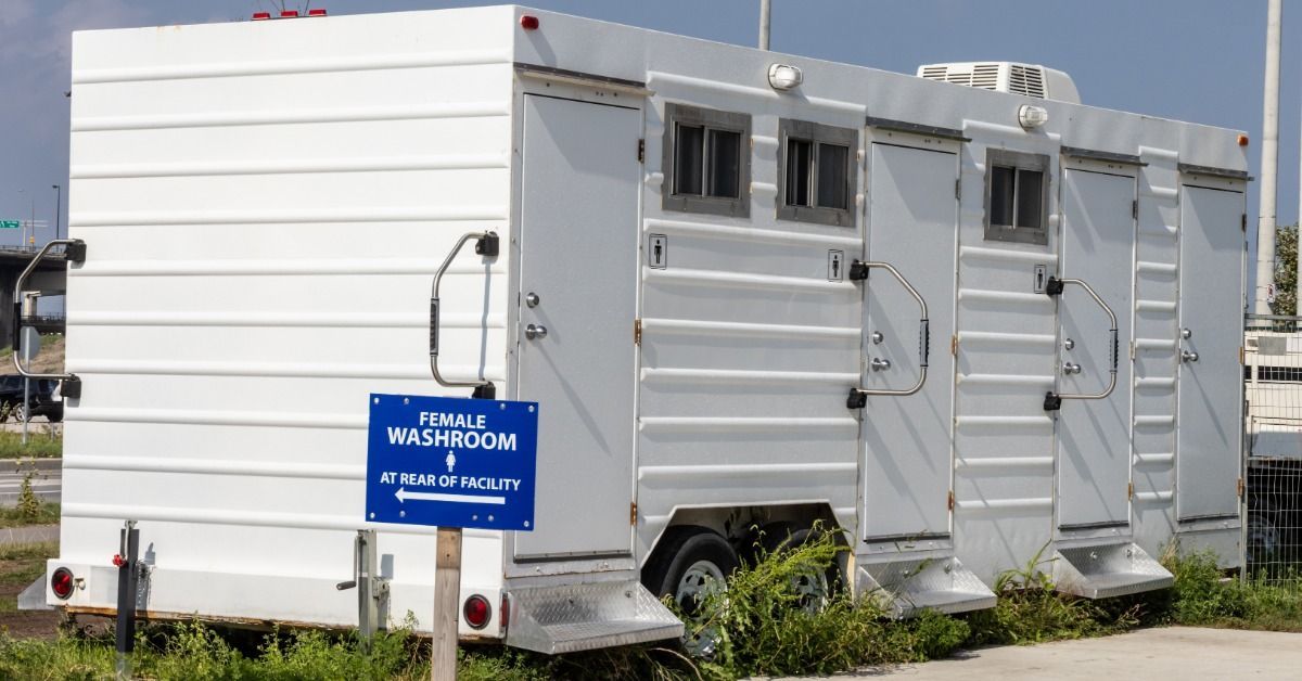 An outdoor event venue with a large, luxury portable restroom trailer unit. There are four doors for