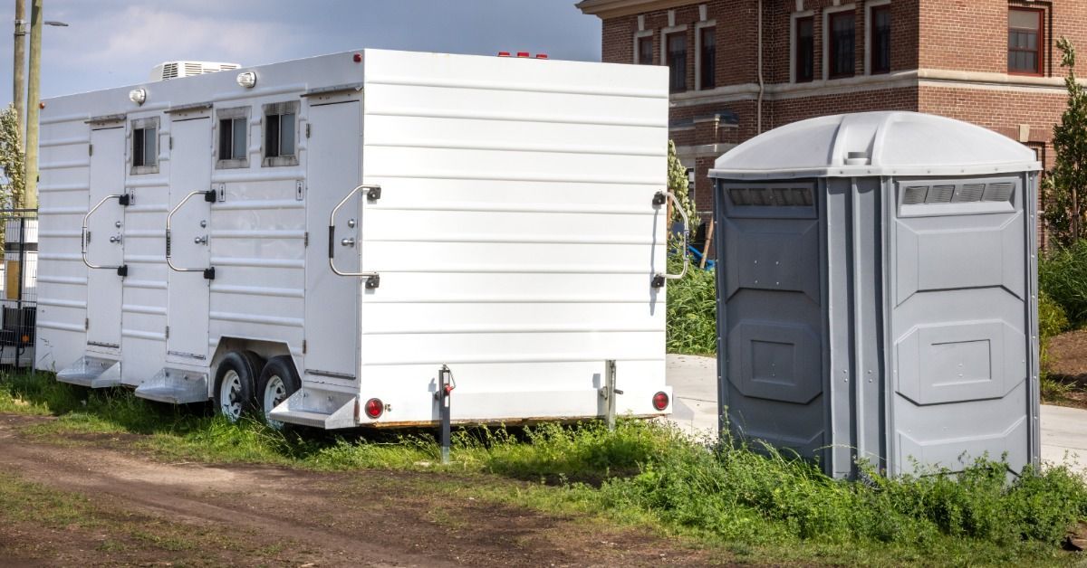 An outdoor corporate event with a luxury bathroom trailer next to a regular single-unit porta potty.