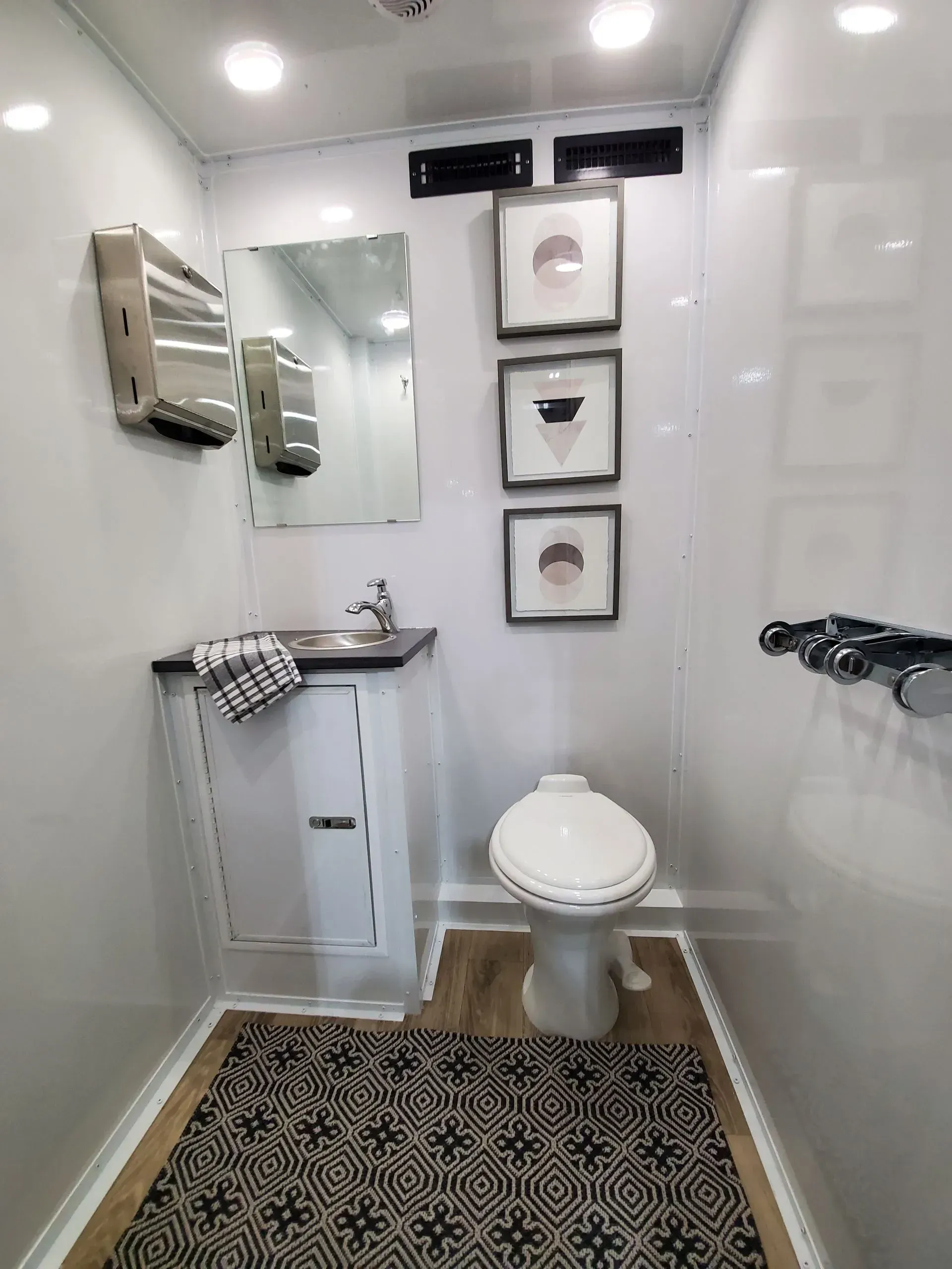 Luxury portable restroom interior with pedestal toilet, sink, mirror, and decorative artwork in Oran