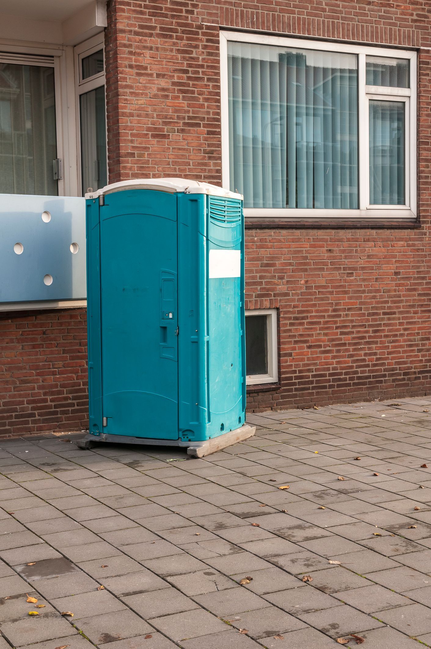 A blue portable toilet on a brick sidewalk, ideal for outdoor events and emergency situations.